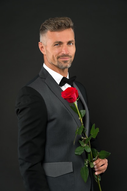 Feliz día de la mujer. Hombre elegante con rosa roja en el día de la mujer. Hombre guapo con traje formal y pajarita negra celebrando el día de la mujer. 8 de marzo o celebración del día internacional de la mujer.