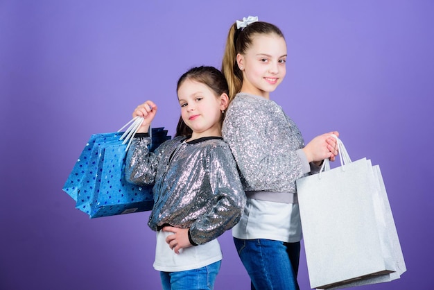 Feliz día del niño Hermanas pequeñas compras en línea Ventas y descuentos Hermandad y ahorros familiares en compras Asistente de tienda de moda infantil con paquete Niñas pequeñas con bolsas de compras