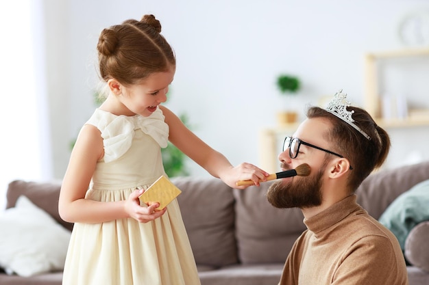 Feliz día del padre, la hija del niño en la corona maquilla a papá y se ríe.