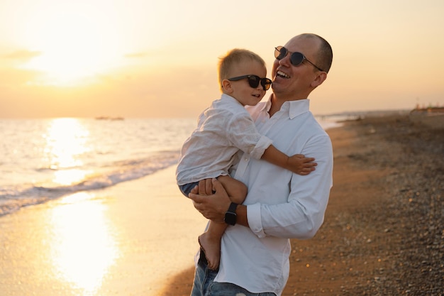 Feliz día del padre Padre y bebé juegan en la playa Papá y él Niño juntos disfrutando del atardecer Padre soltero cariñoso abraza a su pequeño hijo lindo