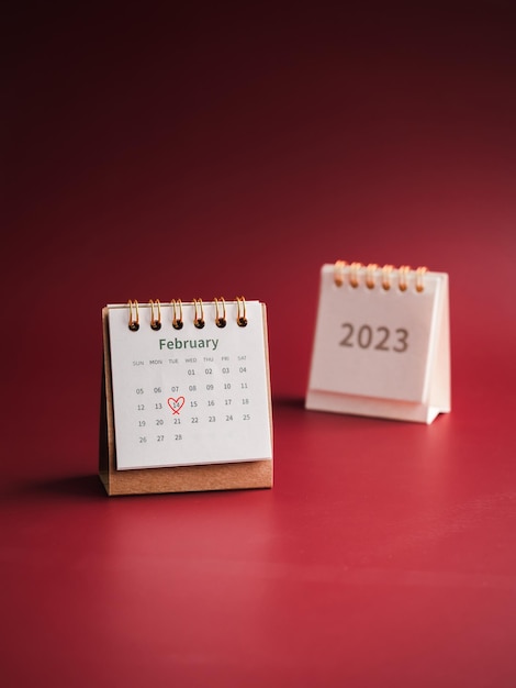 Feliz día de San Valentín, escritorio de calendario de febrero de 2023 sobre fondo rojo estilo vertical El corazón rojo dibuja una marca de mano el día 14 en el calendario de mesa blanca con el mes de febrero con los números del año 2023