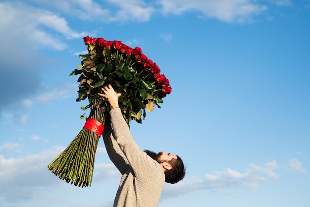 Feliz día de San Valentín. Hombre guapo dando flores a su amante el día de San Valentín. Hombre que sostiene un elegante ramo de rosas rojas.