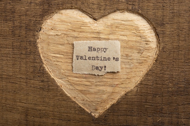 Feliz día de San Valentín pequeña nota de texto escrita cerca del concepto de saludos del Día de San Valentín Forma de corazón tallada en madera como fondo para la tarjeta de felicitación de San Valentín