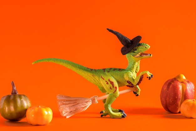 Feliz dinosaurio de juguete verde con sombrero de bruja y escoba sobre fondo naranja Feliz idea de tarjeta de Halloween