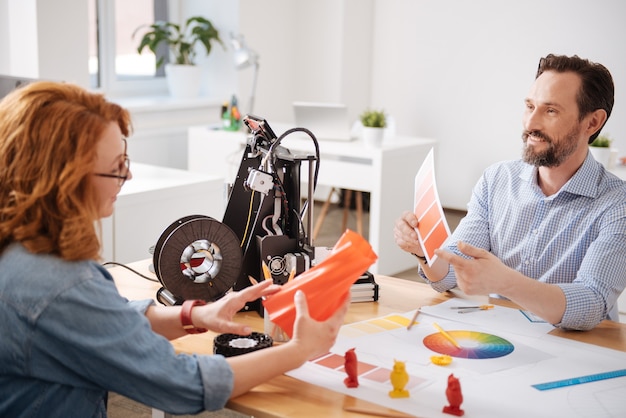 Feliz diseñador masculino creativo apuntando al color naranja y sugiriendo elegirlo mientras consulta con su colega