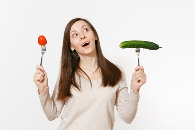 Feliz divertida mujer vegana tiene pepino verde, tomate rojo en un tenedor aislado sobre fondo blanco. Nutrición adecuada, comida vegetariana, estilo de vida saludable, concepto vegetal. Área de publicidad con espacio de copia.