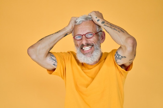 Feliz divertido viejo barbudo hipster hombre con gafas aislado en amarillo