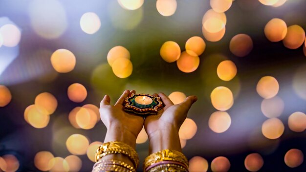 Feliz Diwali - Manos de mujer con henna sosteniendo velas encendidas aisladas sobre fondo oscuro. Lámparas Clay Diya encendidas durante Dipavali, celebración del festival hindú de luces. Copie el espacio para el texto.