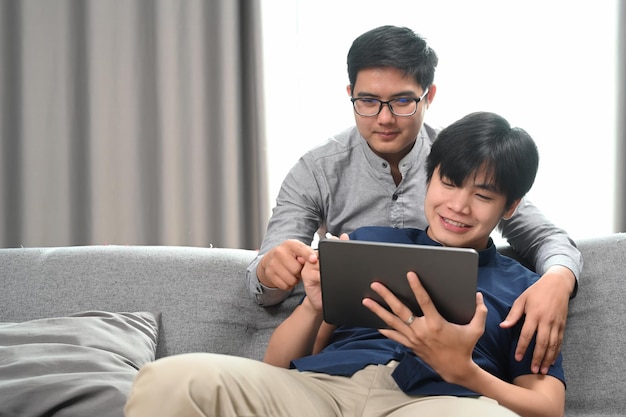 Feliz do casal homossexual abraçando e usando tablet digital juntos na sala de estar Conceito LGBT homossexual