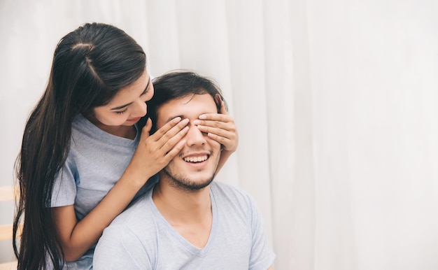 Foto feliz doce casal jovem ela fechando os olhos do namorado na cama no quarto momentos românticos e surpresa