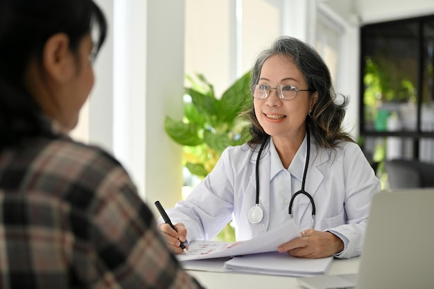 Feliz doctora de edad asiática teniendo una agradable conversación con su paciente en la clínica