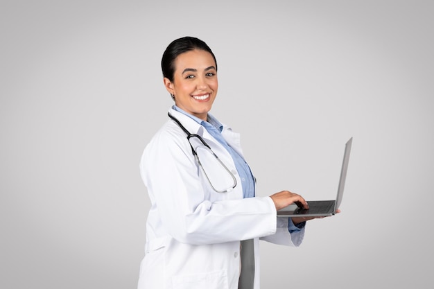 Feliz doctora latina comprometida con una computadora portátil en el fondo del estudio