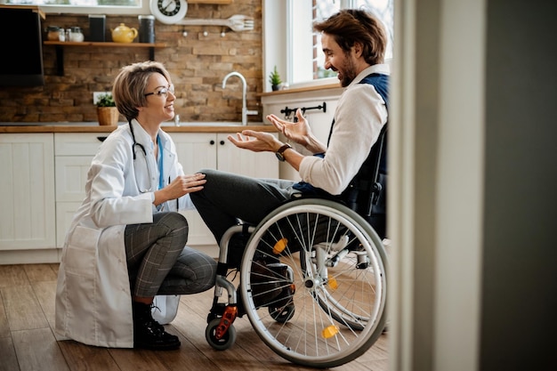 Feliz doctora y su paciente discapacitado en silla de ruedas comunicándose durante la visita a casa.