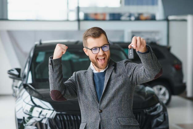 Feliz dono de um carro novo Homem bonito emocional em roupas casuais está feliz comprando um carro na concessionária