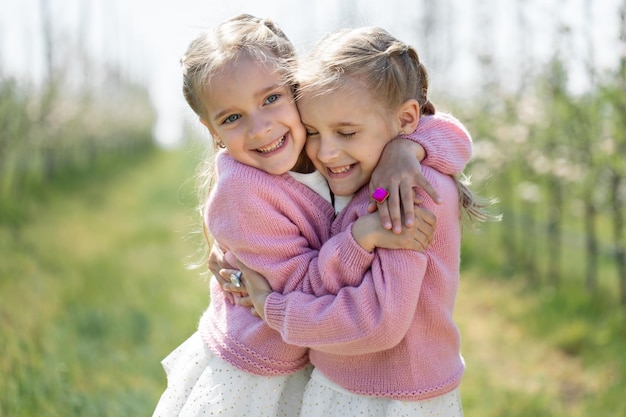 Feliz dos hermanas gemelas se abrazan con el telón de fondo de un huerto de manzanos en flor verde