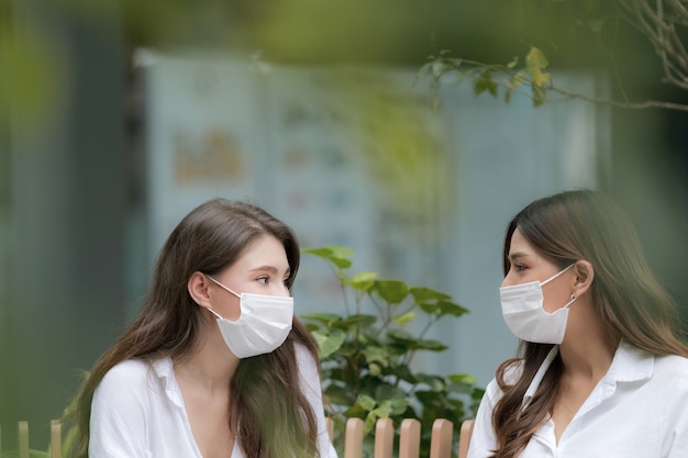 Feliz dos mujer joven con cara sonriente vistiendo mascarilla protectora hablando y riendo con centro comercial de comunicación