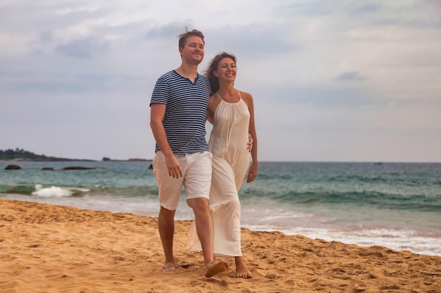 Feliz e adorável casal de família juntos abraçando no fundo do pôr do sol do oceano ao ar livre homem e mulher em roupas casuais andando na praia