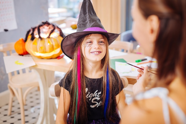 Feliz e alegre. Engraçada, linda garota de cabelos escuros usando fantasia de Halloween, sentindo-se feliz e alegre