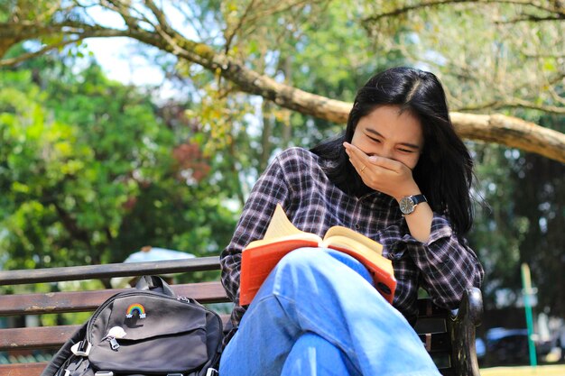 feliz e alegre estudante asiática lendo um livro e rindo aproveitando as férias