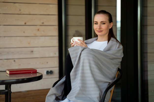 Feliz e alegre jovem bonita gosta de café da manhã e de uma vista da natureza no terraço de um