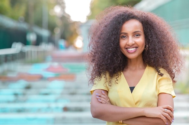 Feliz e alegre mulher negra afro com seu cabelo encaracolado está posando em uma rua vazia Inclui espaço para cópia