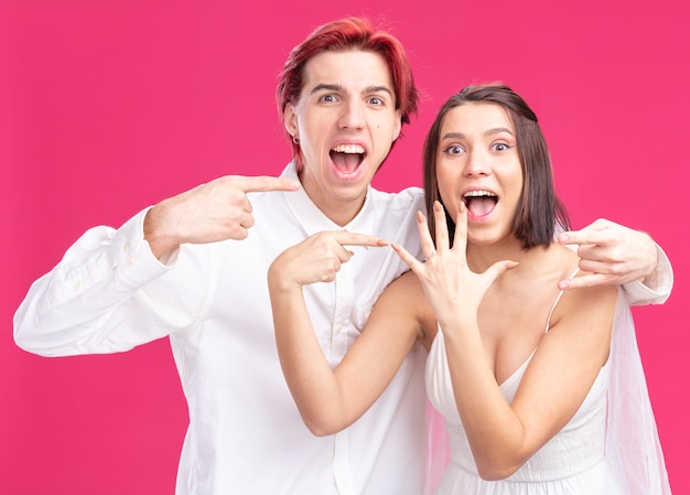 Feliz e animado casal de noivos, noivo e noiva se divertindo, posando juntos, apontando para a aliança de casamento no dedo, felizes apaixonados juntos