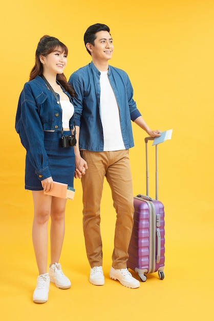 Feliz e animado jovem casal de turistas asiáticos em um fundo colorido amarelo