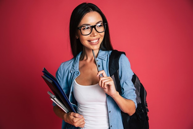 Feliz e animado retrato de uma jovem estudante bonita em óculos com mochila isolada em estúdio