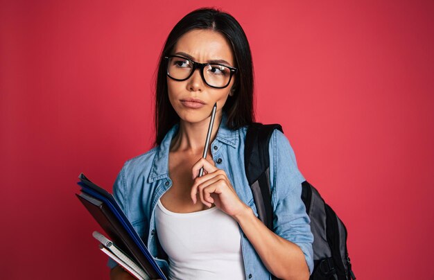 Feliz e animado retrato de uma jovem estudante bonita em óculos com mochila isolada em estúdio