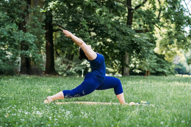 Feliz e confiante sorridente mulher curvilínea fazendo ioga, alongamento, treino de pilates, exercitando-se ao ar livre Jovem modelo plussize fazendo exercícios de aquecimento no parque de verão de manhã cedo