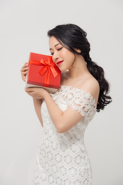 Feliz e elegante mulher asiática segurando uma caixa de presentes especial e vestindo vestido sobre fundo branco