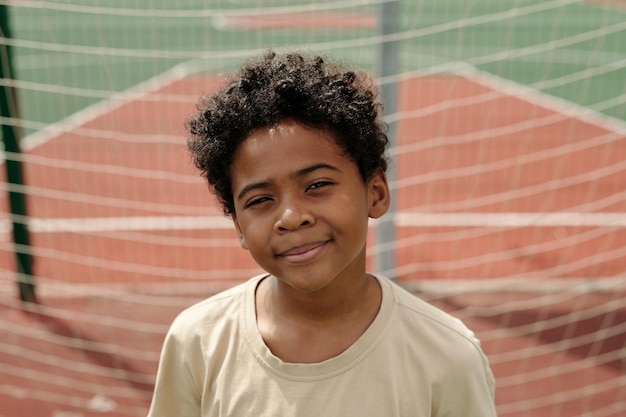 Feliz e fofo estudante afro-americano olhando para a câmera contra a rede do gol