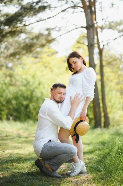 Feliz e jovem casal grávida abraçando na natureza