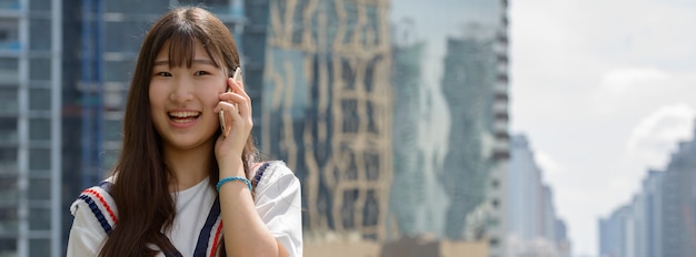 Feliz e linda jovem adolescente asiática falando ao telefone contra vista da cidade