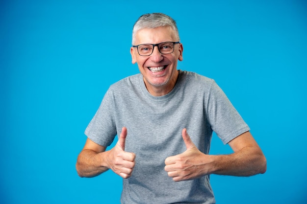 Foto feliz e positivo velho bonito mostra sinal de ok sobre fundo azul