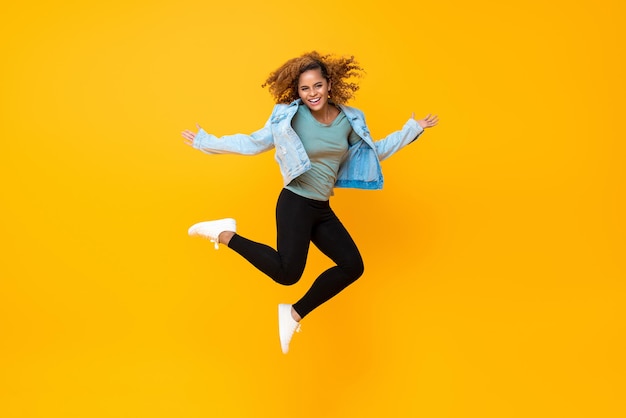 Feliz e sorridente jovem afro-americana pulando isolada em fundo amarelo