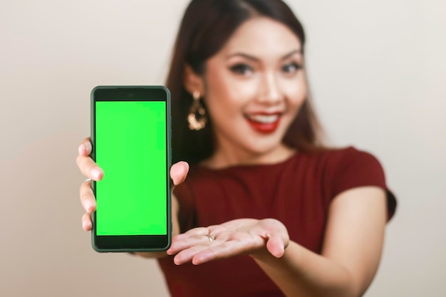 Feliz e sorridente jovem asiática mostrando e apontando para uma tela verde em branco