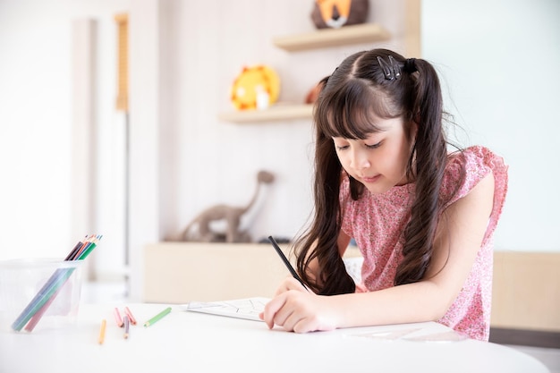 Feliz e sorridente jovem estudante asiática com lápis de cor para fazer uma lição de casa depois da escola