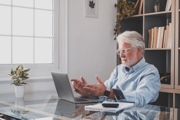 Feliz e velho empresário caucasiano sorrindo, trabalhando on-line, assistindo ao podcast do webinar no laptop e fazendo chamadas em conferência do curso de educação de aprendizagem, faça anotações, sente-se na mesa de trabalho, conceito de elearning