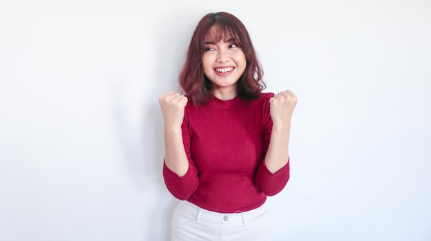 Feliz e vencedora linda garota asiática com camisa vermelha em fundo branco