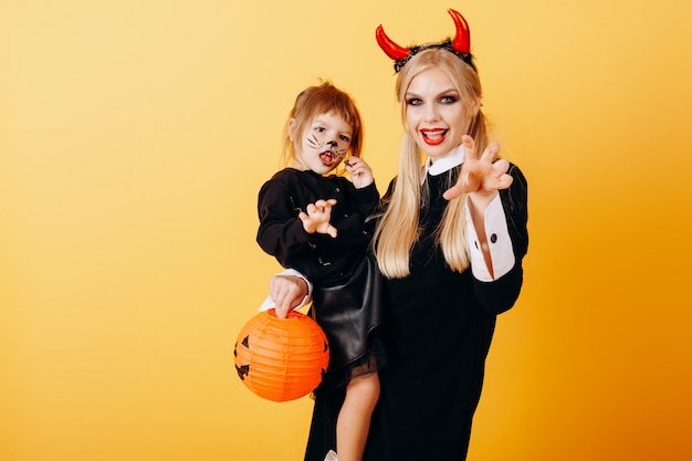 Foto feliz emoción diablo mujer de pie contra un amarillo y sosteniendo a una niña