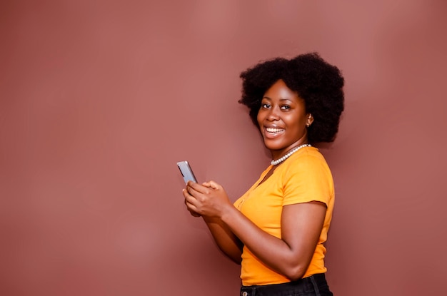 Feliz y emocionada dama afroamericana con peinado afro usando un teléfono móvil en el estudio detrás de un fondo en blanco