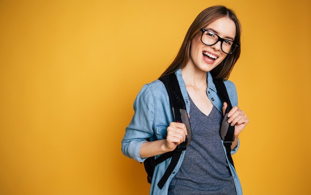 Foto feliz y emocionada linda joven estudiante retrato de niña en gafas con mochila aislada en el estudio