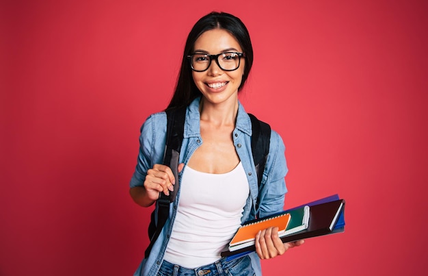 Feliz y emocionada linda joven estudiante retrato de niña en gafas con mochila aislada en el estudio