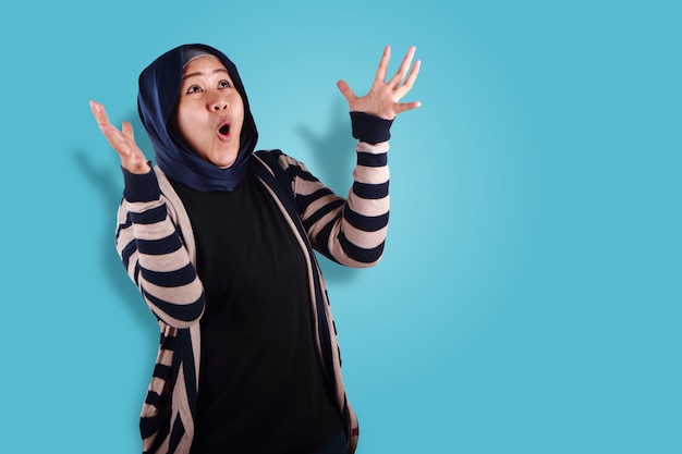 Feliz y emocionada mujer musulmana asiática mirando hacia arriba con las manos levantadas esperando un premio sorprendido desde arriba