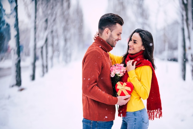 Feliz y emocionada pareja de enamorados se divierten, bailan y se abrazan al aire libre en el parque de la ciudad de invierno mientras celebran el día de San Valentín