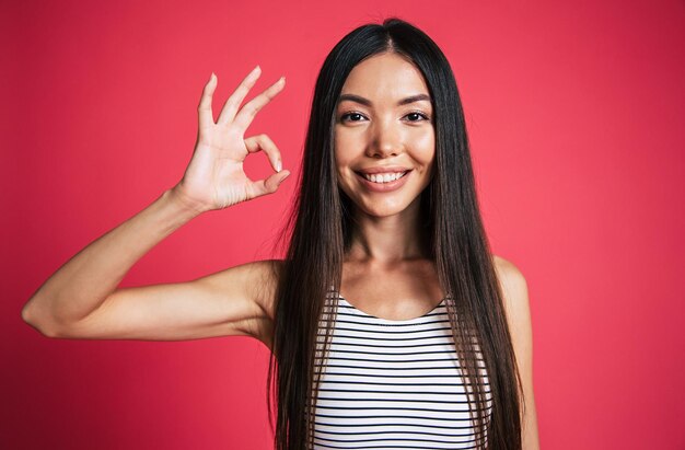 Feliz y emocionado hermoso retrato de mujer asiática joven aislado sobre fondo rosa. Concepto de emociones de personas