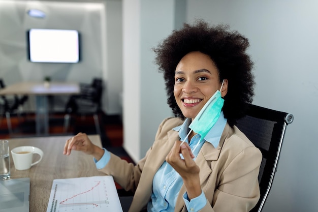 Feliz empresaria afroamericana usando mascarilla protectora mientras trabaja en la oficina