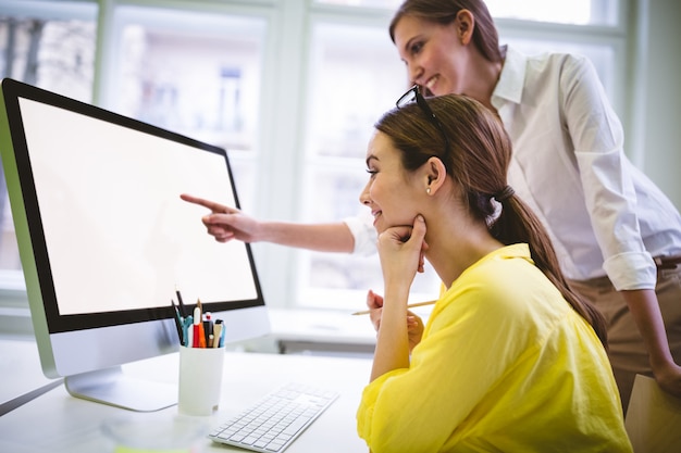 Feliz empresaria apuntando a la pantalla de la computadora al colega en la oficina creativa