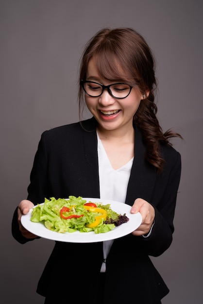 Feliz empresária asiática segurando uma salada enquanto sorri